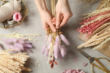 Florist making bouquet of dried flowers at grey stone table, top view