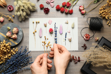 Woman making herbarium of dry flowers at wooden table, closeup - obrazy, fototapety, plakaty