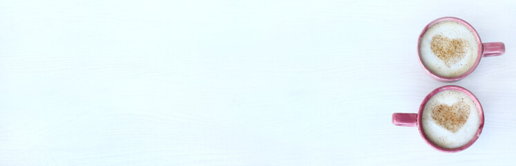 long empty table and two red cups with frothy cappuccino decorated with symbols of hearts top view. warming coffee valentine