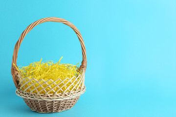 Fototapeta na wymiar Easter basket with yellow paper filler on light blue background, space for text