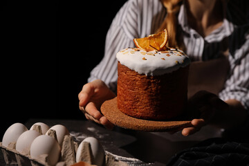 Young woman holding traditional decorated Easter cake on black background, closeup. Space for text