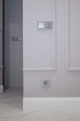 Electrical outlet on brown wall above baseboard and white marble floor. Open invisible hidden door in wall with boiserie in classic interior