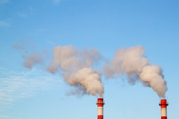 Smoking industrial stacks in thermal power plant emit polluted air into atmosphere in blue sky