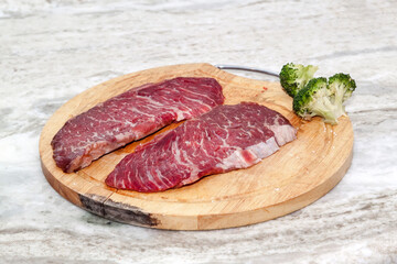 boneless beef steak and fresh broccoli on marble table. Meat and vegetables close up on wooden chopping board on quartzite countertop