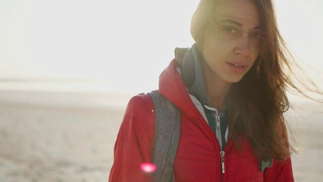 slow motion closeup portrait of Young adult mixed raced woman traveler meeting sunrise at sea beach. millenial hipster girl in red jacket with wind blowing hair enjoing scenery landscape