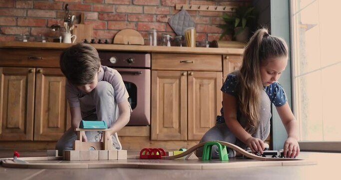 Happy small adorable children siblings playing with wooden toys, building tower and railroad together on warm floor in kitchen, leisure free time kids domestic activity, hobby pastime concept.