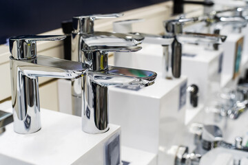 An assortment of washbasin faucets in a plumbing store. Chrome plated metal products. Close-up
