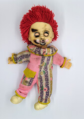 scary and old battered clown doll with burnt face and red hair on the background of white color top view