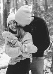 
A man hugs a woman and she smiles against the background of a pine snow forest black and white photo