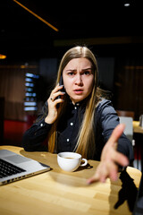 Young woman holding a cup of coffee and using laptop computer talking on the phone. Businesswoman working from home. Work from home