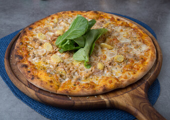 Pizza with chicken meat, onion, baby corn and rocket leaves on wooden pizza plate 