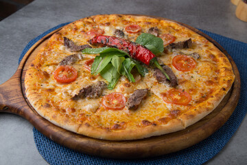 Pizza with sausage, cheese, baby corn, rocket leaves and roasted red pepper on wooden pizza plate 