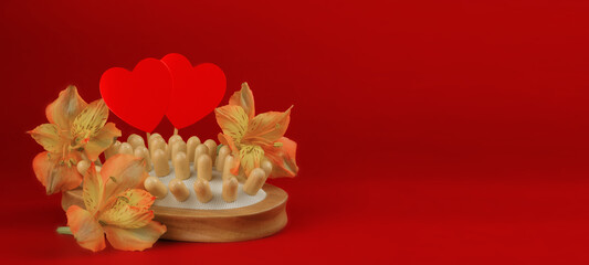 Obraz na płótnie Canvas Wooden massage brush for skin with flowers and hearts, on a red background. Valentine's day concept. Banner. Copy space