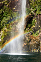 Waterfall in Milford Sound, New Zealand, with two rainbows, rocks and greenery