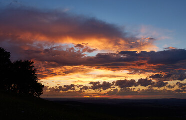 Sunset with blue sky and orange-gray clouds, the trees and meadow in the foreground are barely visible as a silhouette. Germany.
