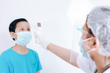 Nurse or doctor checks boy body temperature using infrared forehead thermometer (gun) for virus...