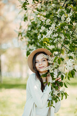 Young beautifull woman near bird cherry flowers. Bloomy bird cherry tree and happy woman in a hat. Spring time card.