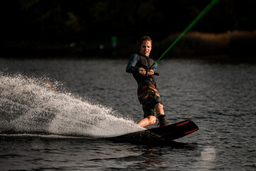 Fototapeta premium athletic man in wetsuit masterfully balancing and riding on wakeboard fast on splashing river water