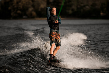 young man in black life jacket holds bright green rope and rides wakeboard