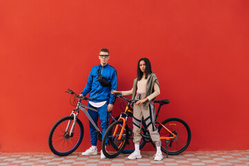 Sports couple in sportswear with bicycles stand on the background of a red wall and look at the camera. Cycling.