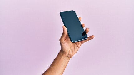 Hand of young hispanic man showing smartphone over isolated pink background.