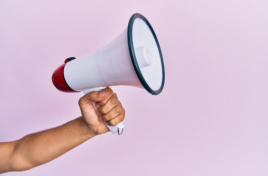 Hand of hispanic man holding megaphone over isolated pink background.