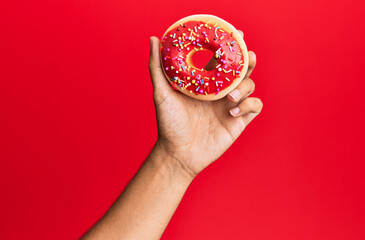 Hand of hispanic man holding donut over isolated red background.