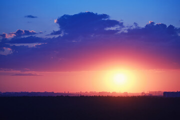 Beautiful setting red sun behind town houses and blue clouds