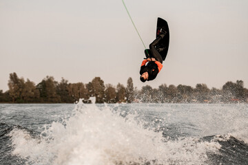 active sportsman skilfully jumps and makes flip over the water on wakeboard