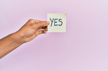 Hand of hispanic man holding yes reminder paper over isolated pink background.