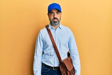 Middle age man with beard and grey hair wearing delivery courier cap puffing cheeks with funny...