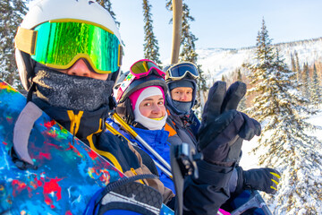 Two boys and one girl ride on a chairlift in mountains. Winter day ski resort. The girl is focused