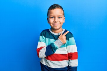 Little kid boy wearing striped sweater smiling cheerful pointing with hand and finger up to the side