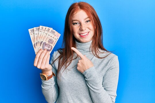 Young red head girl holding 500 mexican pesos banknotes smiling happy pointing with hand and finger