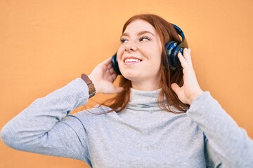 Young irish teenager girl smiling happy listening music using headphones at the city.