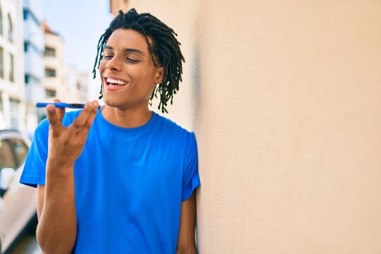 Young african american man sending audio message using smartphone at street of city.