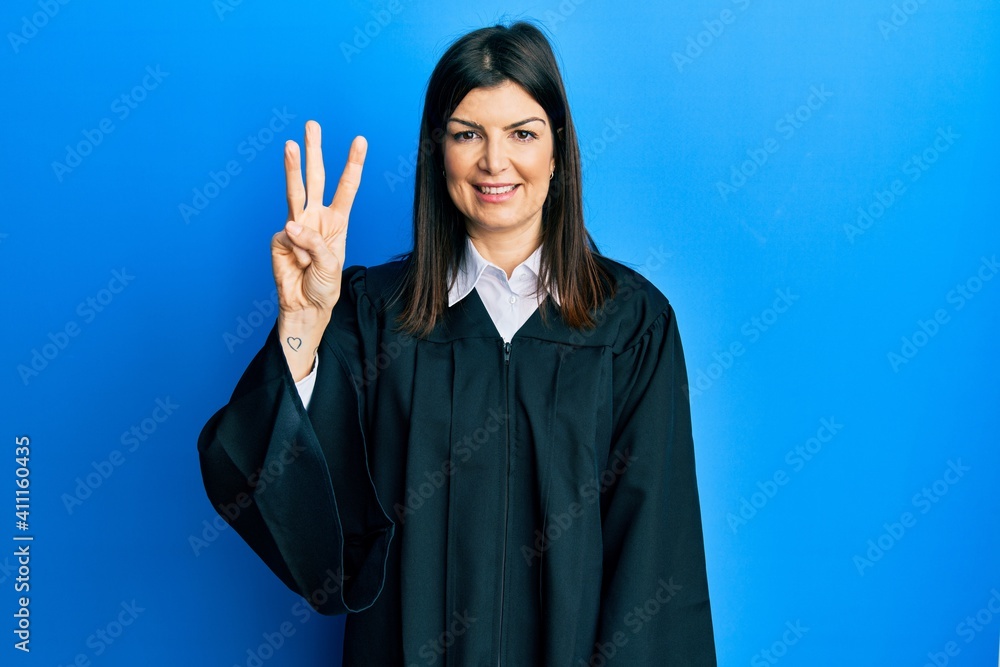 Wall mural young hispanic woman wearing judge uniform showing and pointing up with fingers number three while s