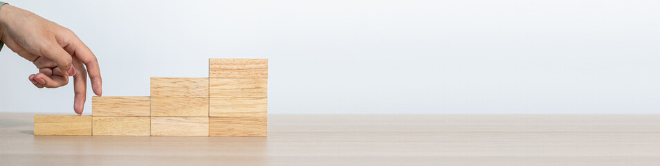 A business woman's hand is walking on a wooden block placed in steps from low to high. The concept of doing business on risk using a wooden block in comparison.