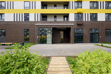 Typical modern entrance to the staircase of an apartment building. Path, lawn with plants in front...