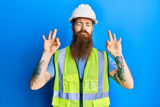 Redhead man with long beard wearing safety helmet and reflective jacket relax and smiling with eyes closed doing meditation gesture with fingers. yoga concept.