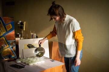 Woman pouring melted wax into amber candles container. Ecological and vegan business. Soya wax candle accessories. Handmade with love. Remote work, online shop, workplace