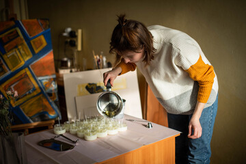 Woman pouring melted wax into amber candles container. Ecological and vegan business. Soya wax candle accessories. Handmade with love. Remote work, online shop, workplace