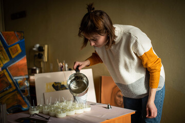 Woman pouring melted wax into amber candles container. Ecological and vegan business. Soya wax...