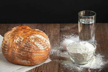 Large round loaf with bread products on wooden table