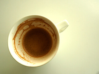 An almost empty cup of coffee with stain is on white table.   Top view.