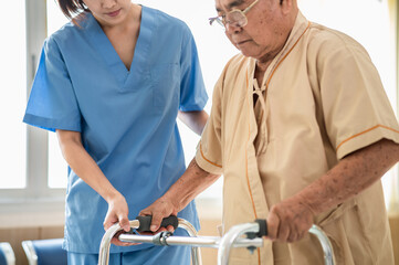 Asian elderly male patient using walking frame with female nurse assistance. Medical professional...
