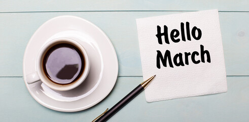 On a light blue wooden tray, there is a white cup of coffee, a handle and a napkin that says HELLO MARCH.