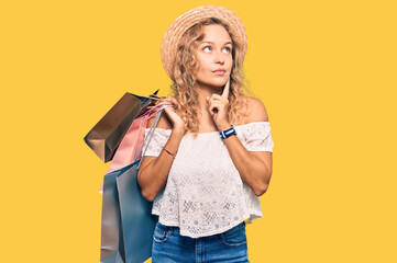 Beautiful caucasian woman holding shopping bags serious face thinking about question with hand on...