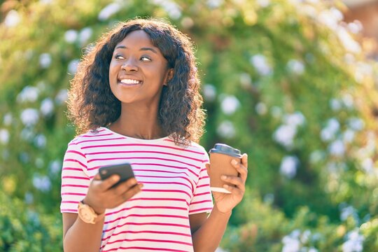 Young african american girl using smartphone drinking coffee at the park.