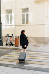 Beautiful woman in black dress on a background of an urban landscape with a suitcase